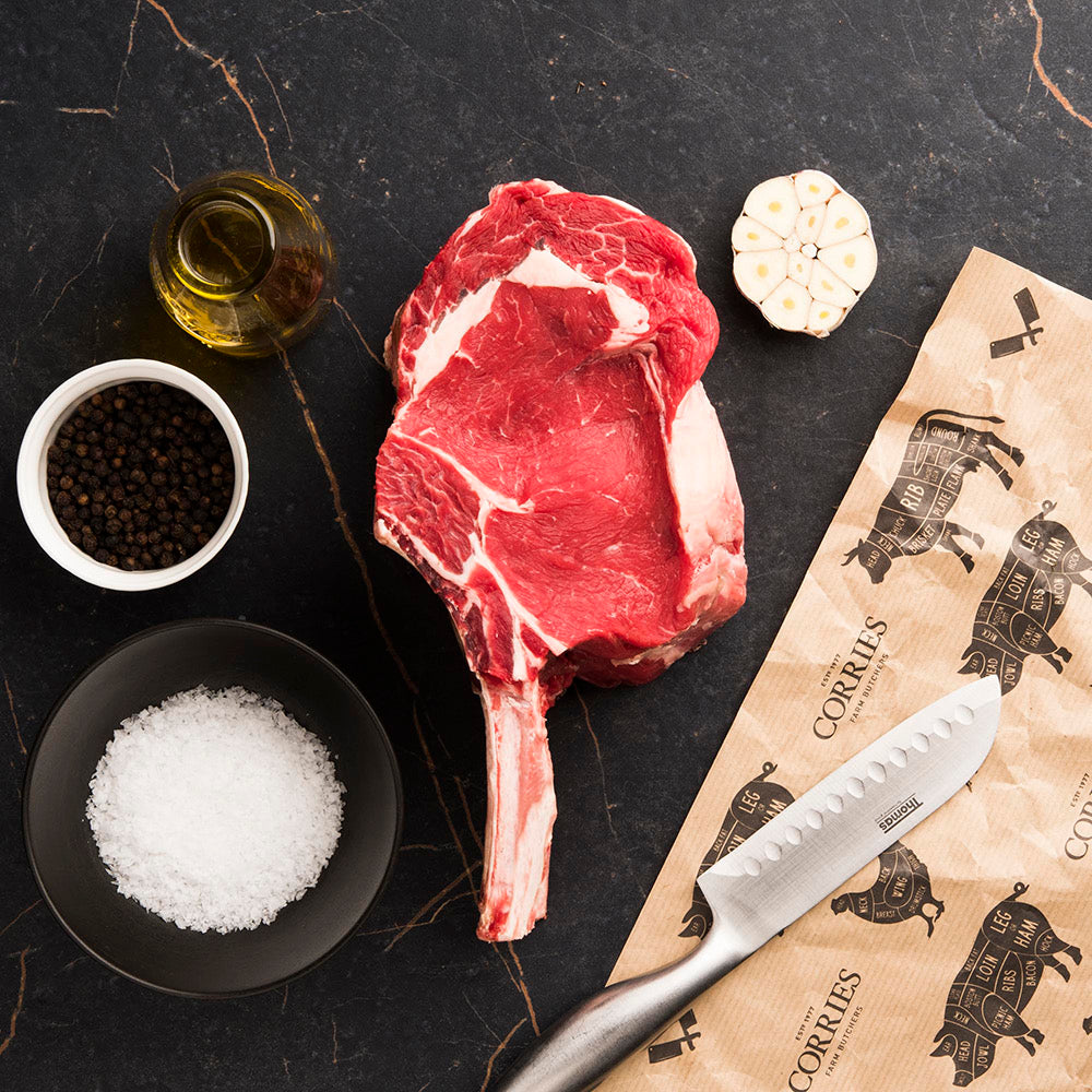 Tomahawk Steak on surface with sea salt, peppercorns